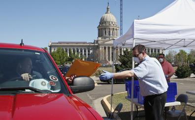 A masked and gloved man takes an envelope from a man in a car in front of a capitol building