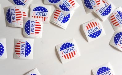 Scattered red white and blue "I voted" stickers across a white background