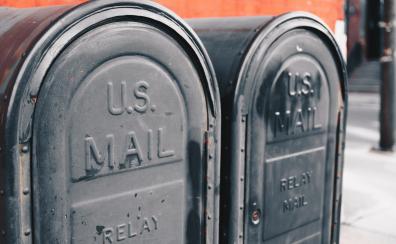 A photograph of two blue U.S. postal boxes against a red brick background