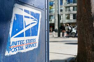 A close-up of a USPS box on a city street